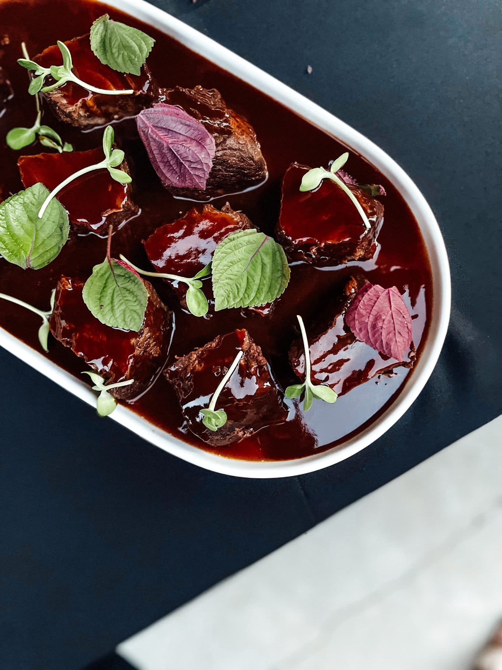 A shared serving platter of braised beef in red wine jus with fresh herbs