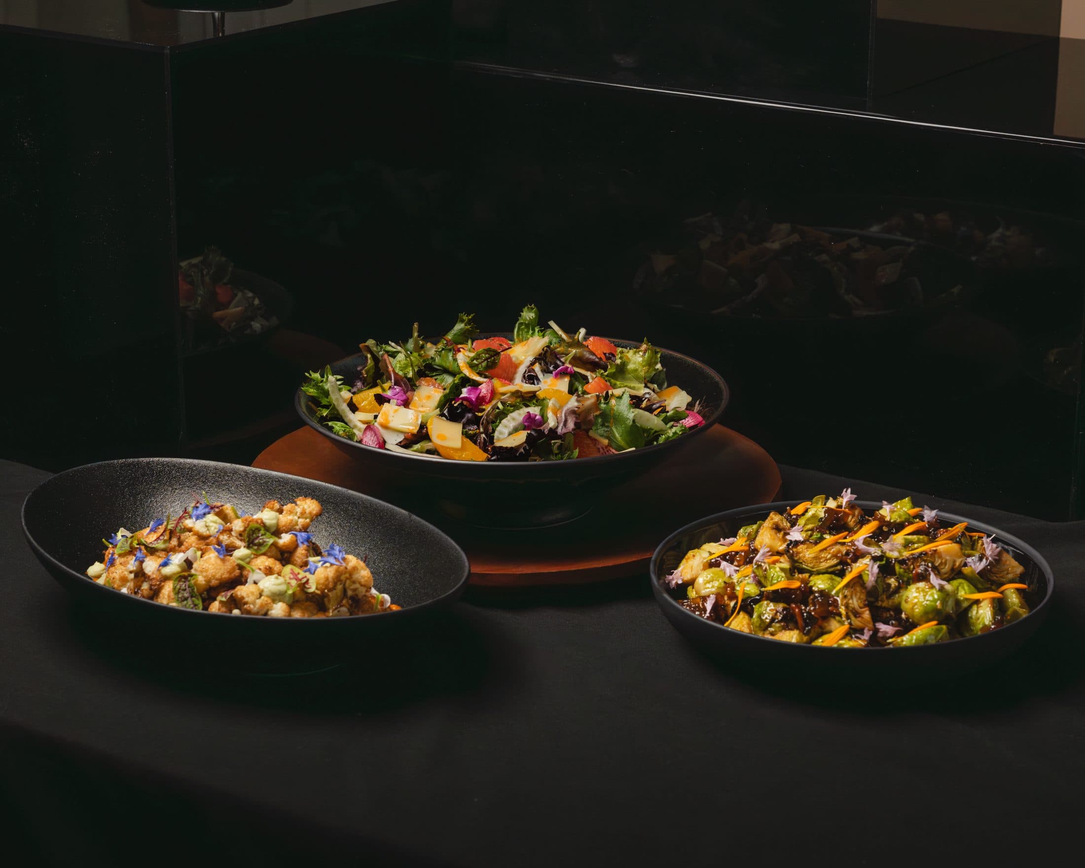 A buffet table set with shared bowls of salad, crispy cauliflower and glazed brussels sprouts